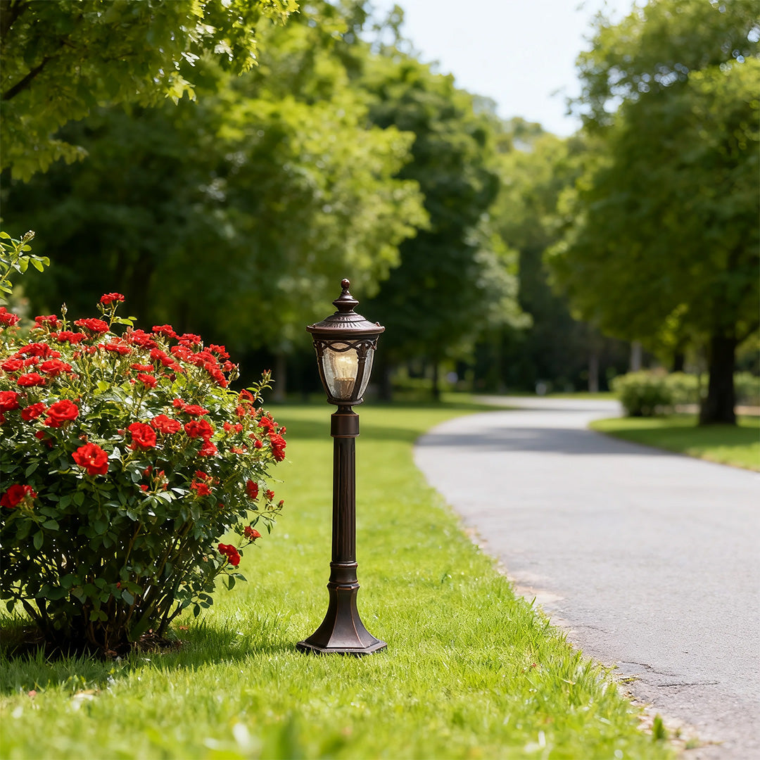 Outdoor light bollard brightening curved driveway edge with red flowers and manicured greenery