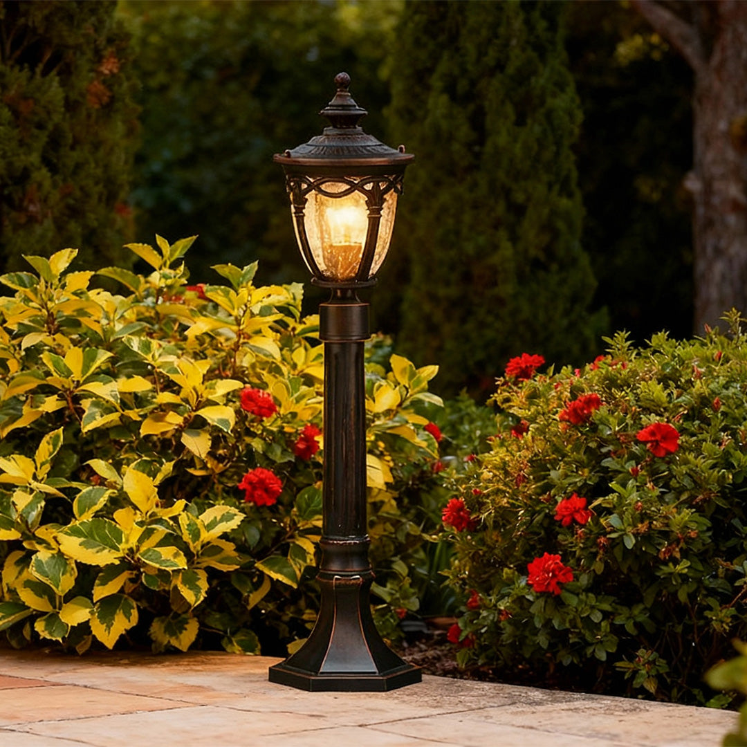 Outdoor light bollard illuminating garden bed with colorful yellow and red flowers at dusk