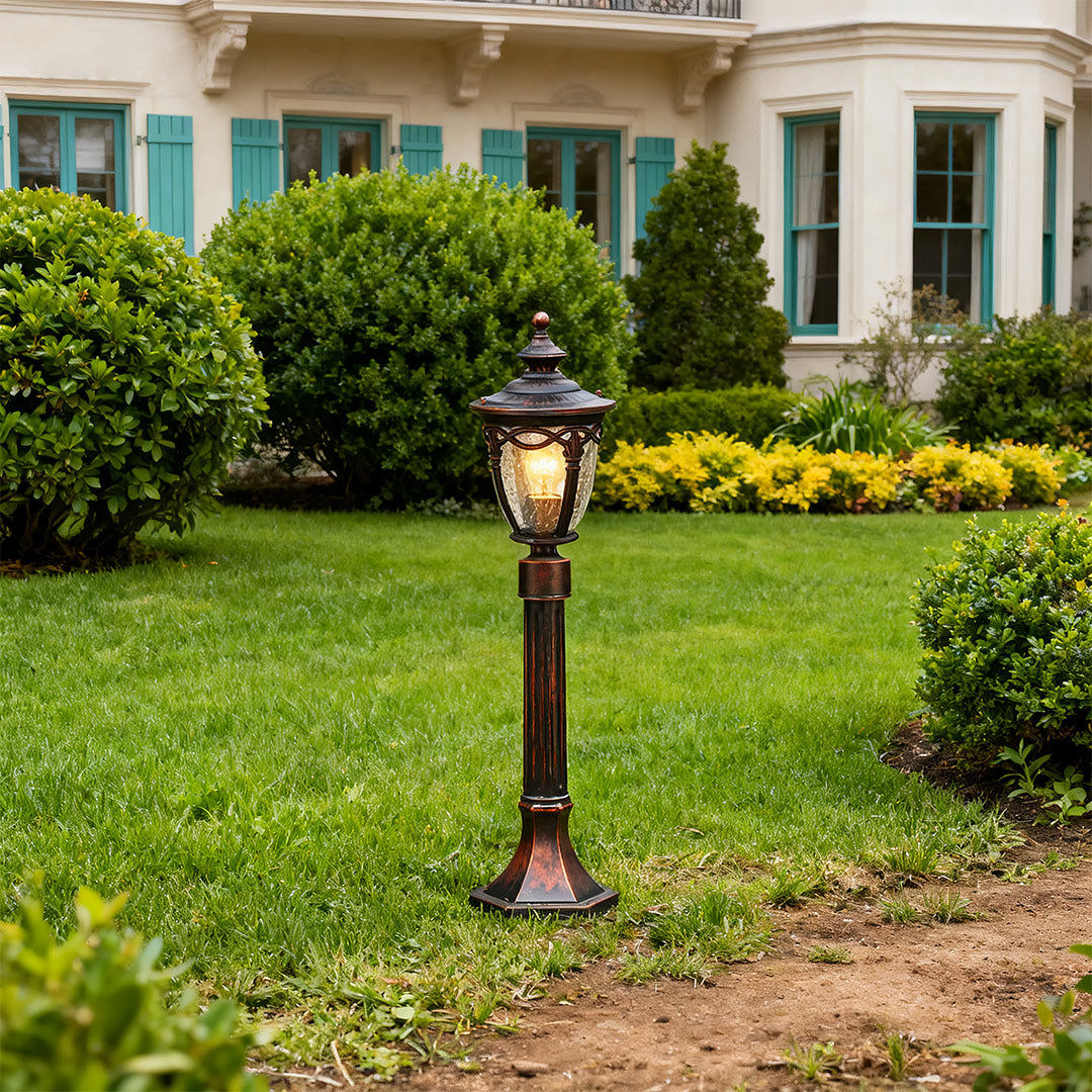 Outdoor light bollard positioned on lawn near white home with green shrubs and mulched bed