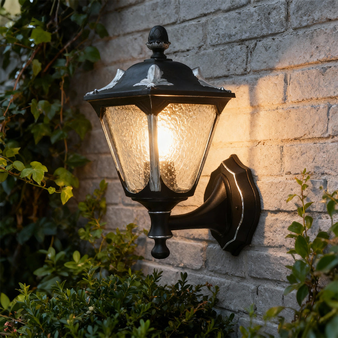Outdoor light for wall providing amber glow on textured brick wall at evening with plants