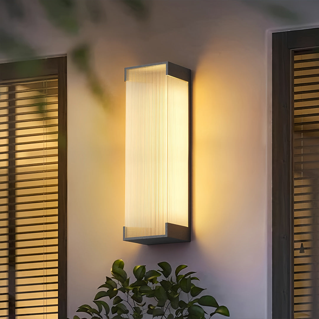 Contemporary gold outdoor lighting fixtures wall mounted illuminating a garden corner with warm ambient glow and ribbed panels.