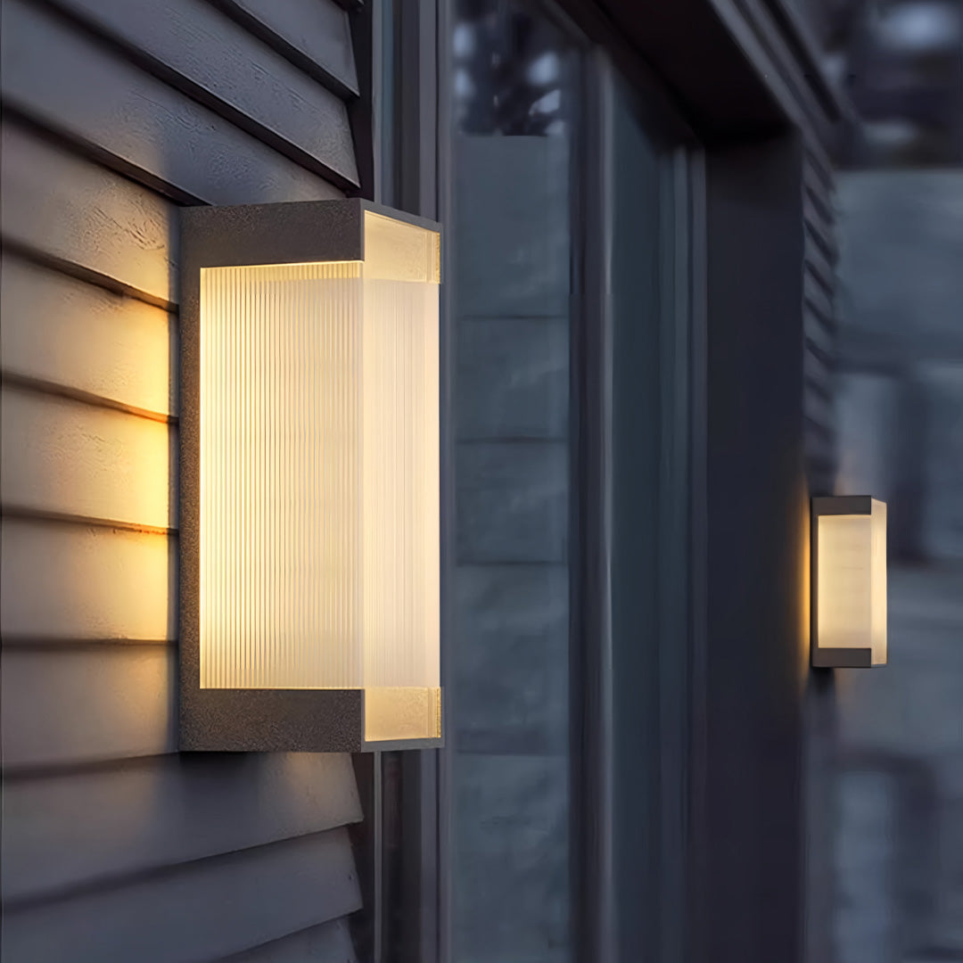 Outdoor lighting fixtures wall mounted in gold finish placed on a wood-textured exterior wall emitting warm layered light.