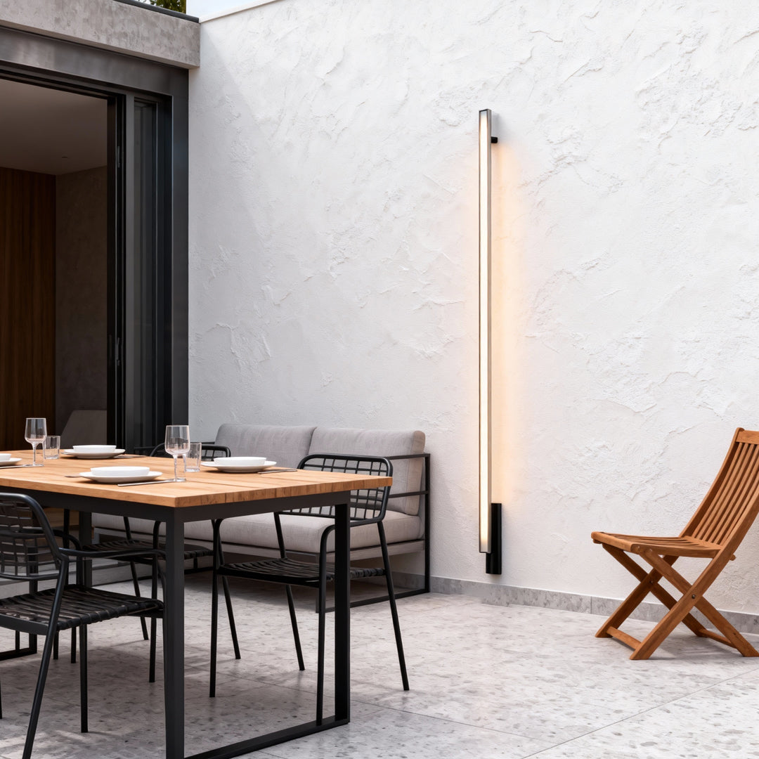 Warm modern outdoor lights wall sconces illuminating a white exterior wall beside an outdoor dining setup.