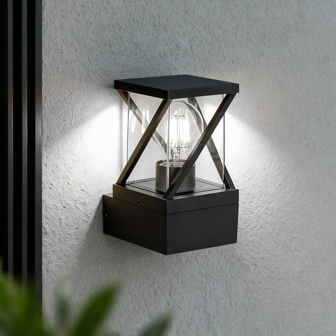 Black lantern-style outdoor modern wall sconce shining warm light against a stucco wall surface.