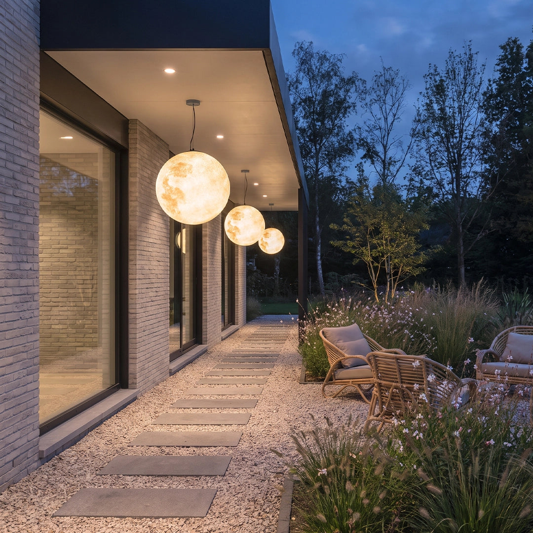Outdoor moon lamps suspended along a covered garden walkway beside a modern home at dusk.