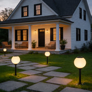 Outdoor path light globe illuminating a modern house entrance with warm directional glow.
