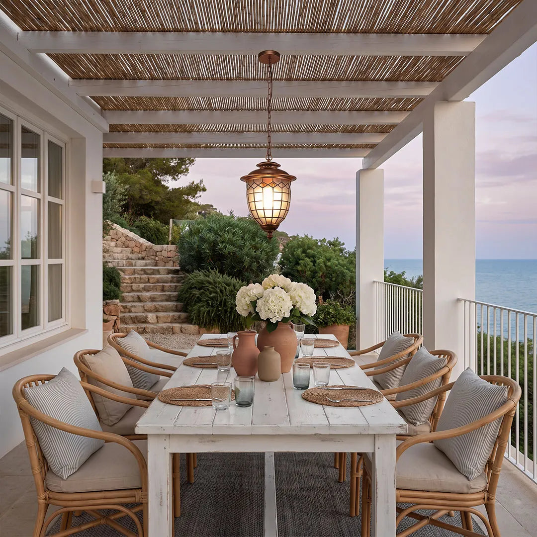 Outdoor pendant lighting fixtures suspended above a coastal-style patio dining area with woven chairs.