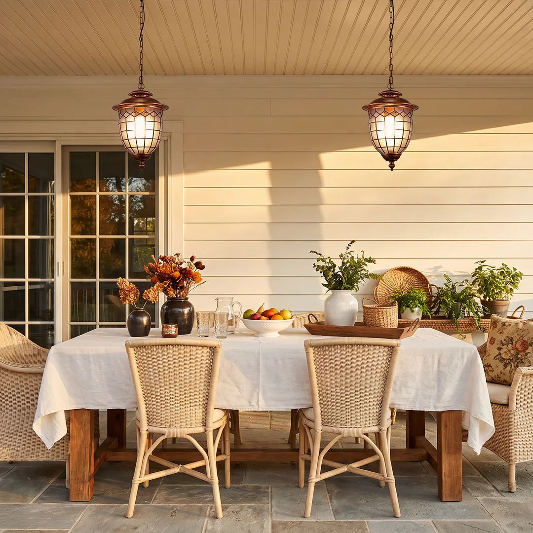 Outdoor pendant lighting fixtures hanging above an outdoor dining table on a bright covered porch.