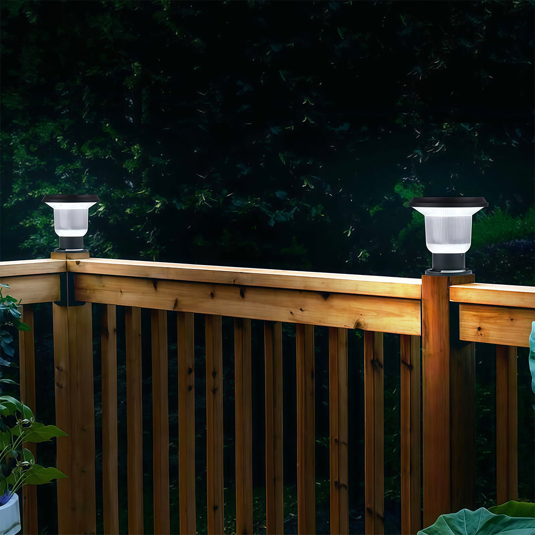 Outdoor pillar light providing soft, warm illumination along a stone pillar fence in a garden.
