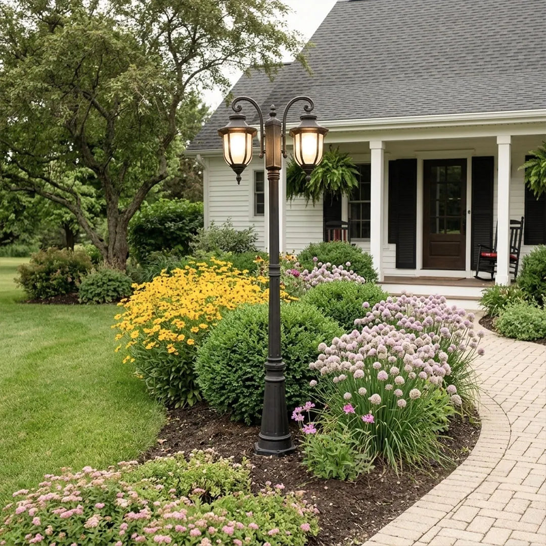 Outdoor post light fixture beside a curved front walkway surrounded by colorful flowers and shrubs.