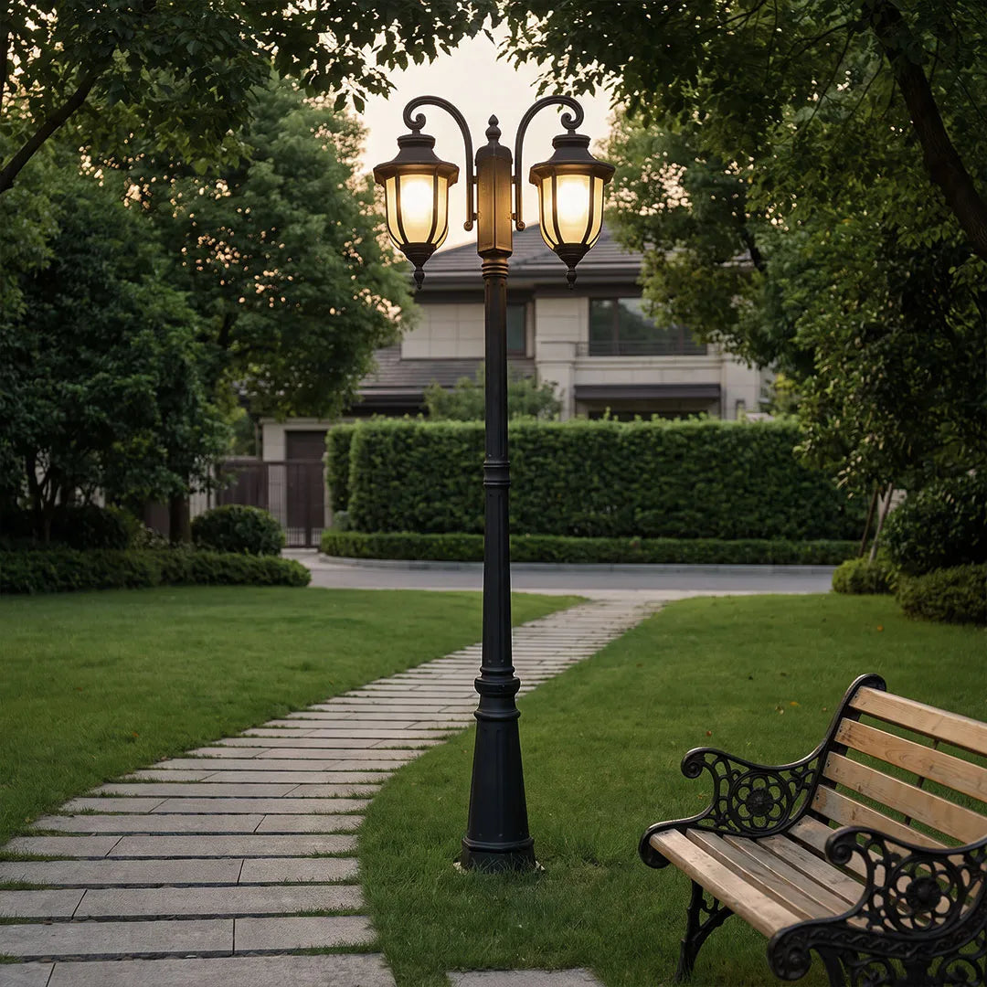 Outdoor post light fixture illuminating a garden path near a bench at dusk.