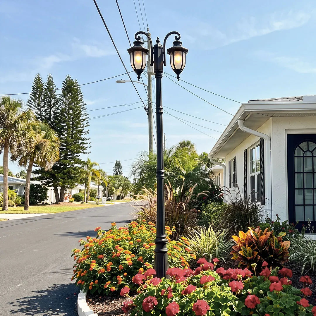 Outdoor post light fixture installed along a roadside flower bed in a residential landscape.