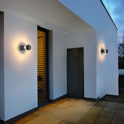 Minimalist black outdoor sconces lights mounted near an entryway on a white modern house wall.