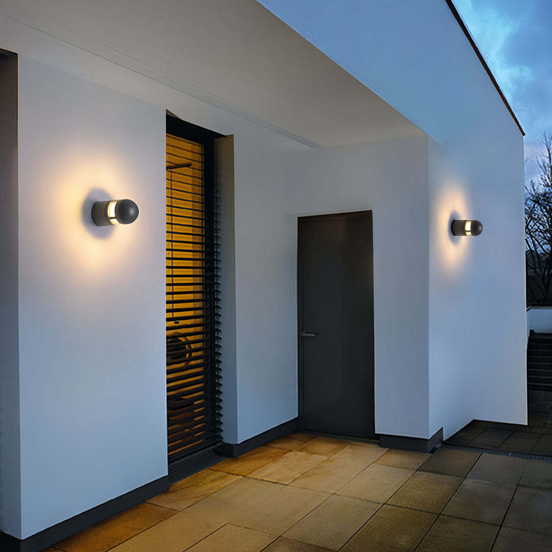 Minimalist black outdoor sconces lights mounted near an entryway on a white modern house wall.