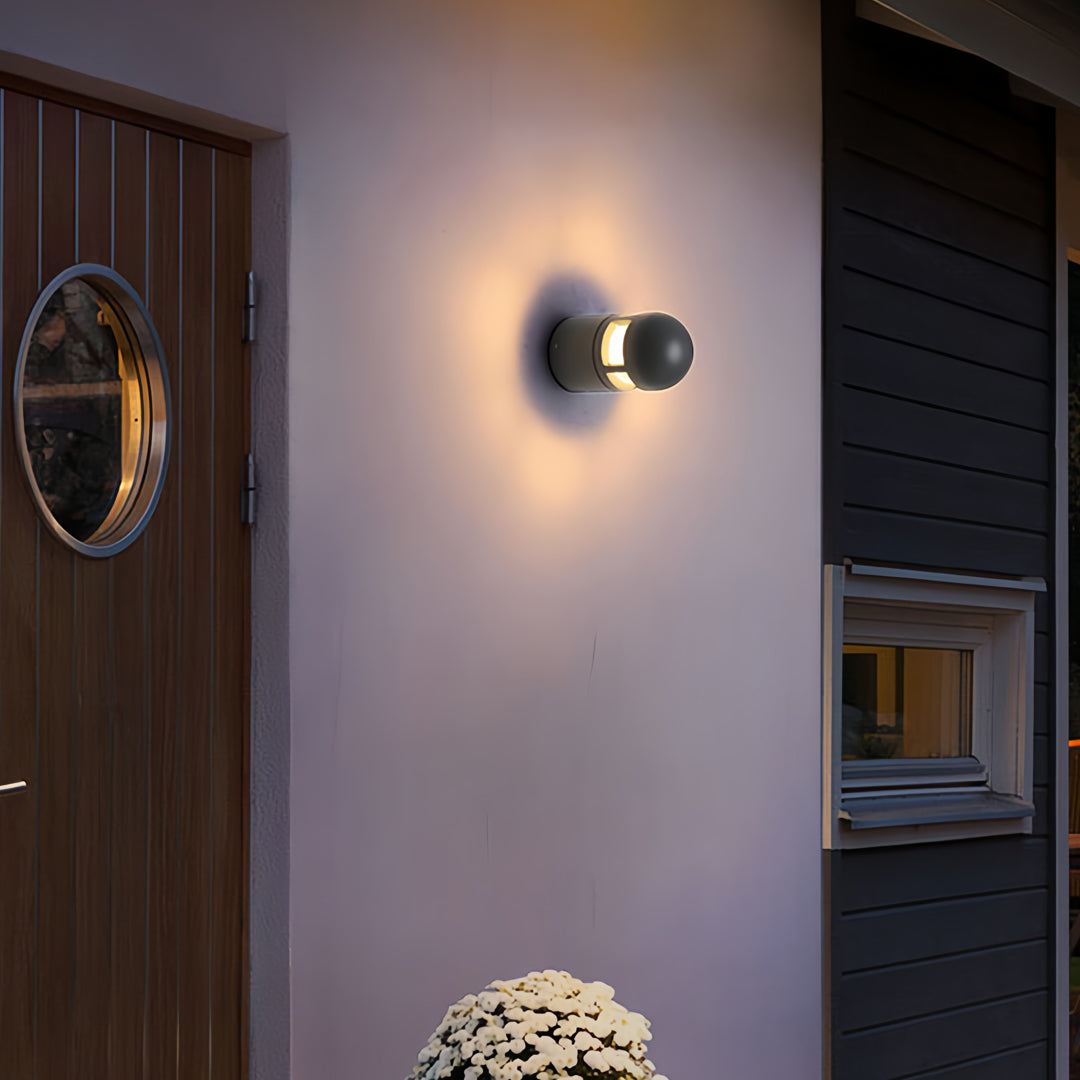 Warm glowing outdoor sconces lights mounted beside a wooden door on a white exterior wall.