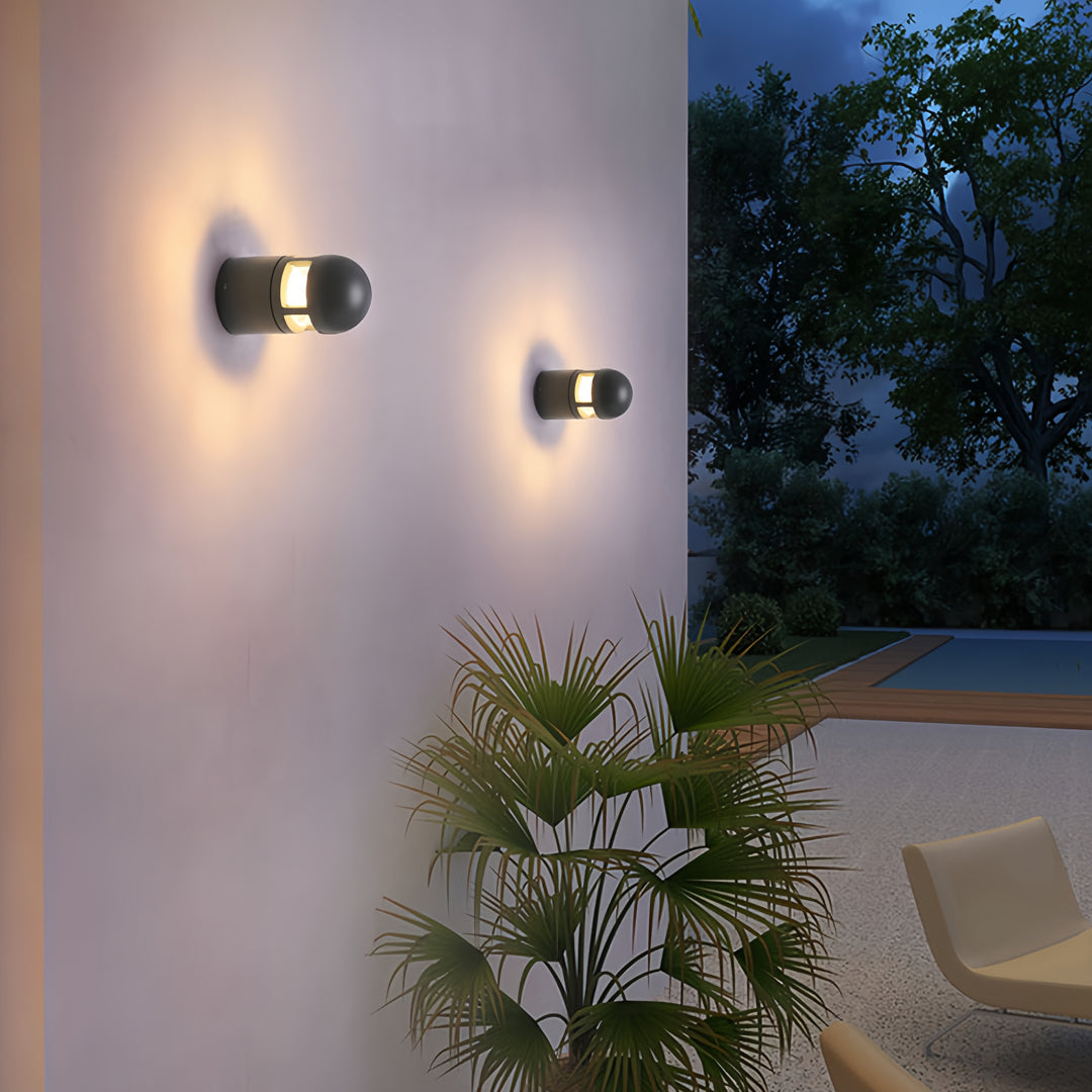 Black modern outdoor sconces lights illuminating a garden area on a white exterior wall at night.