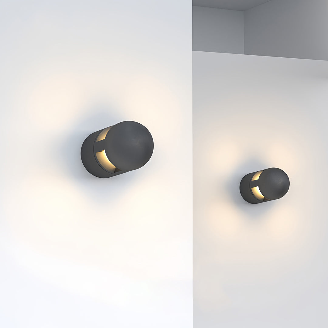 Two modern circular outdoor sconces lights casting warm glow against a bright neutral background.