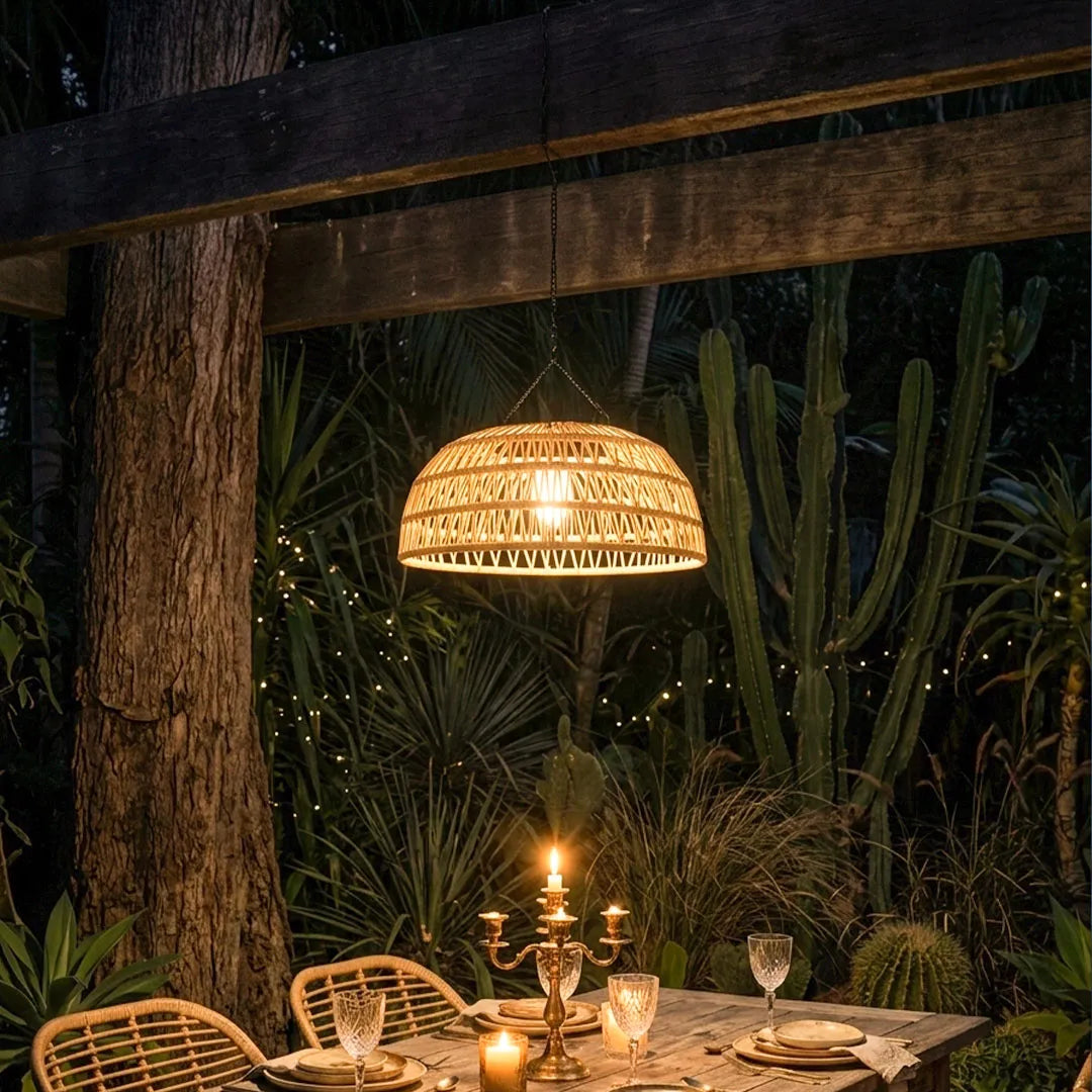 Outdoor solar pendant light hanging under a pergola with a woven rattan shade and warm evening glow.