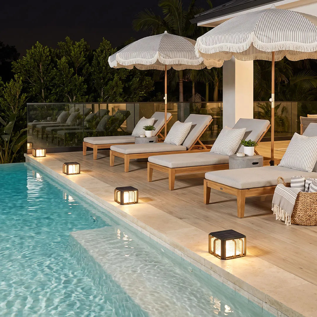 Outdoor solar pillar lights placed beside a swimming pool with a modern architectural design.