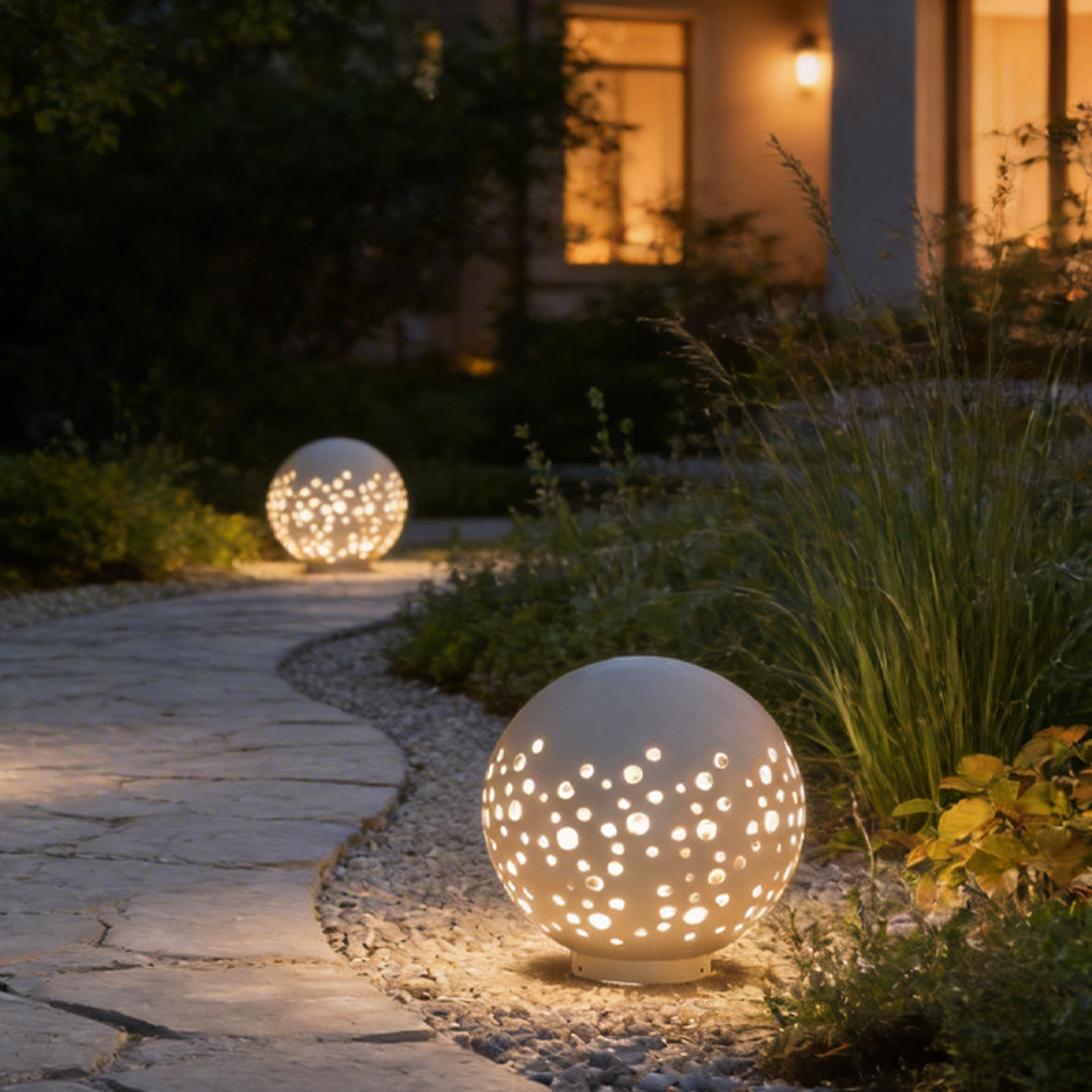 Outdoor sphere light with a perforated design, illuminating a garden pathway at night.