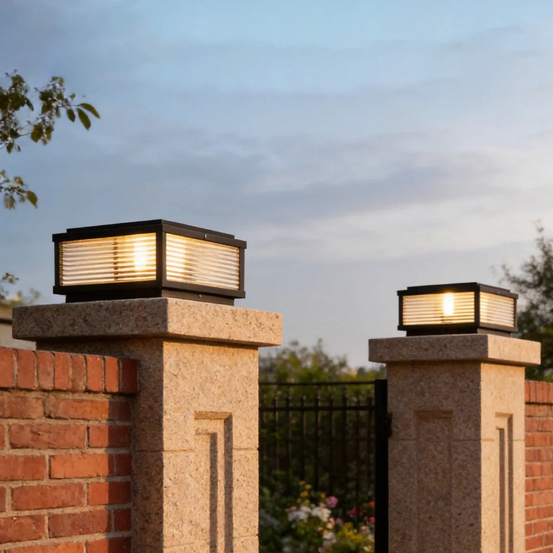 Outdoor square pillar lights on brick entry columns at a residential gate entrance.