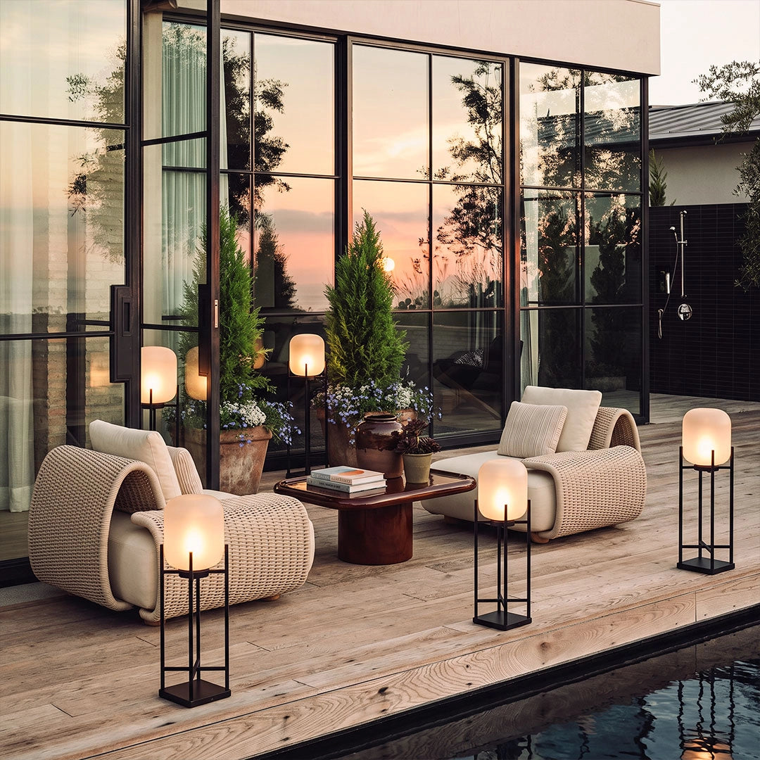 Outdoor standing lights with frosted shades and black metal frames illuminating a modern patio lounge beside the pool at dusk.