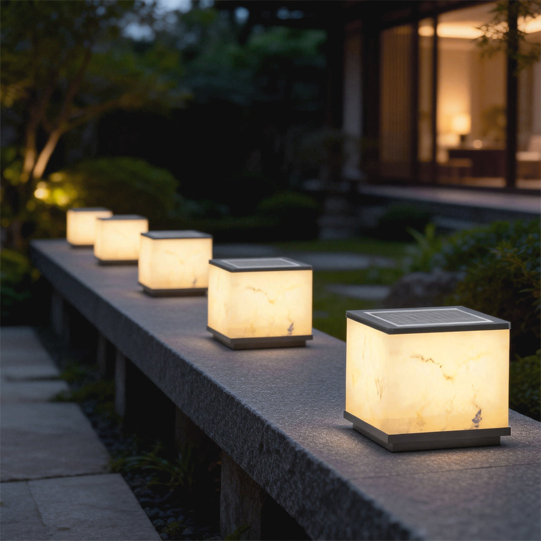 Outdoor stone pillar lights lined along a garden fence, providing soft illumination for a tranquil evening.