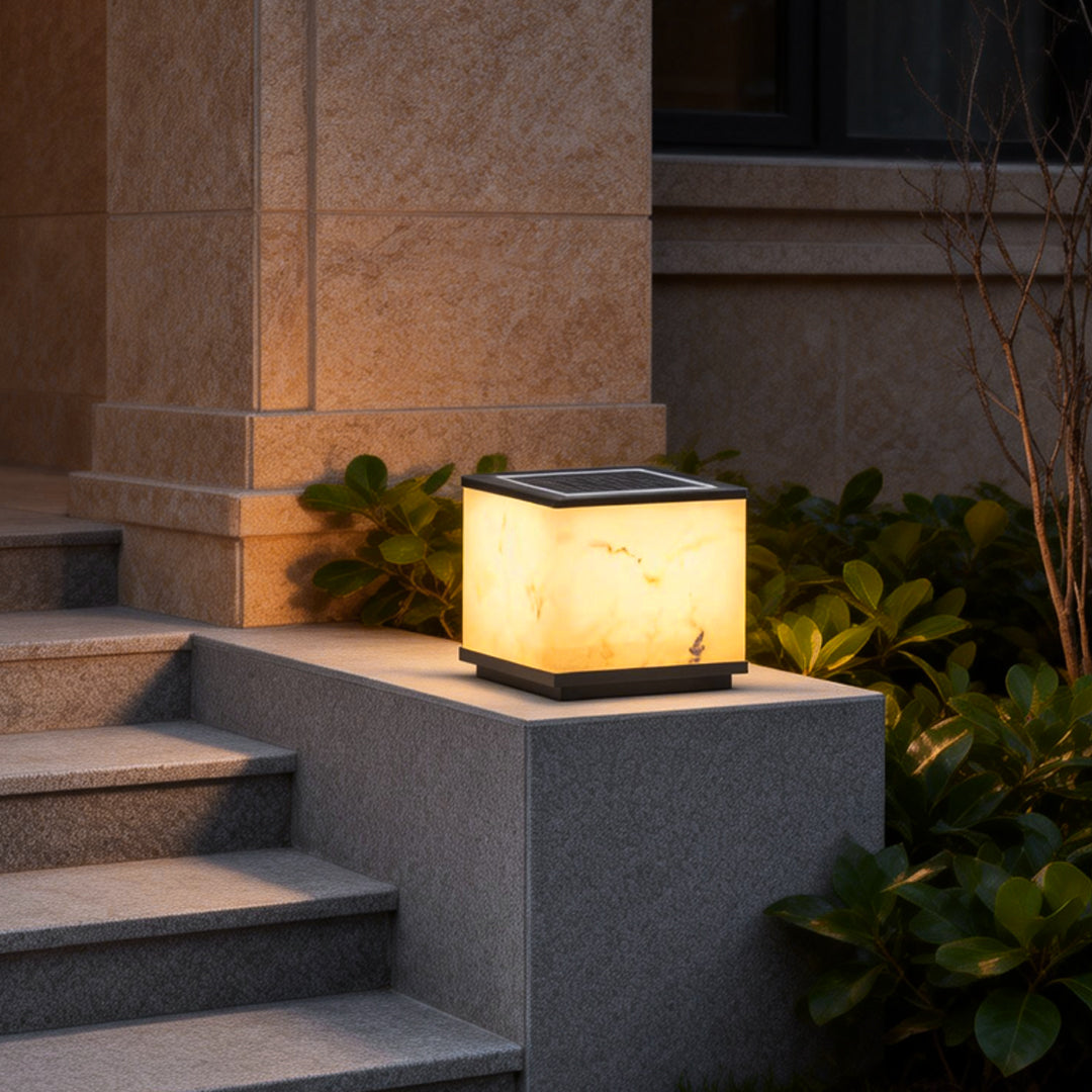 Outdoor stone pillar lights with a warm glow, mounted on stone steps near a modern building entrance.