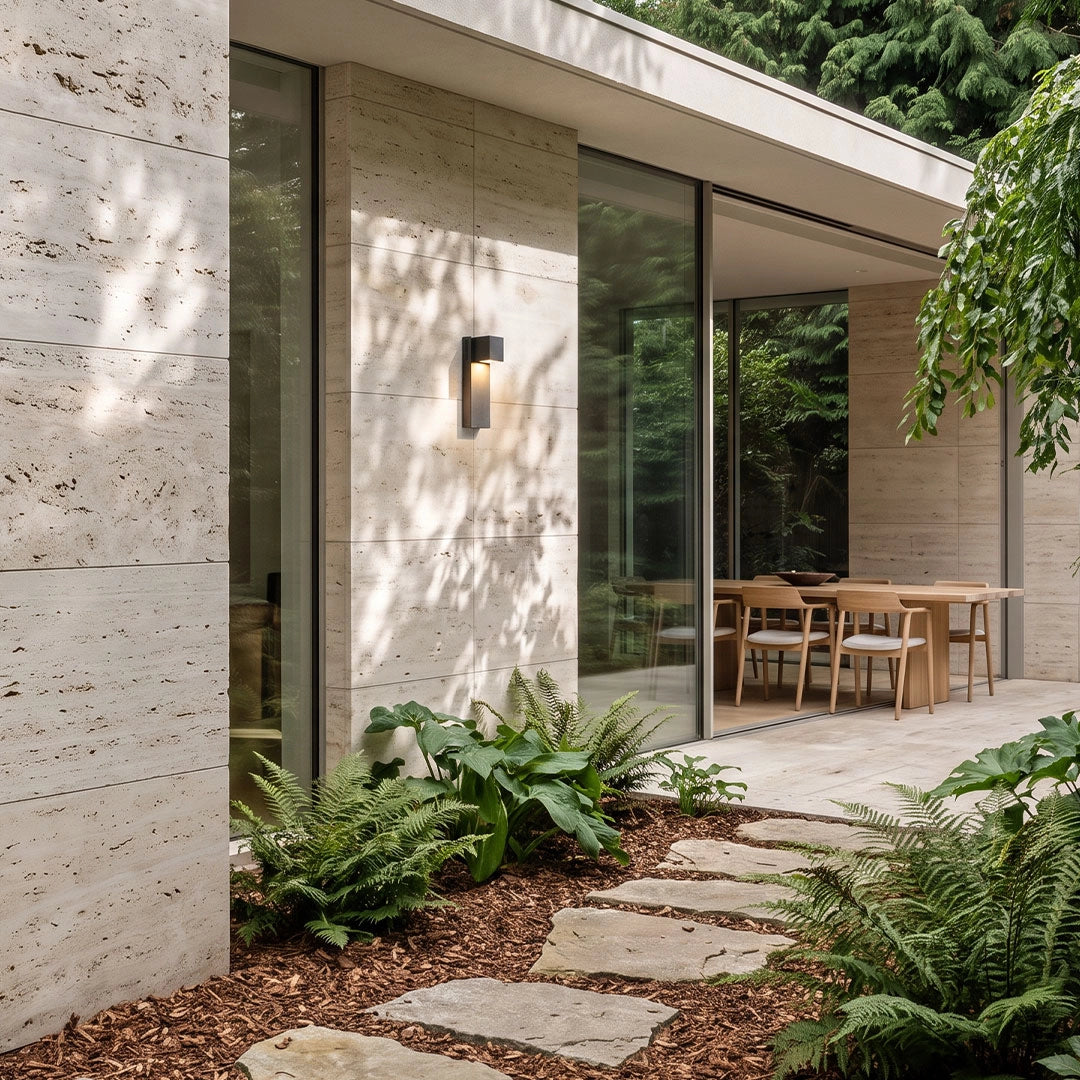Outdoor stone wall lighting in a light stone finish illuminating a walkway beside a contemporary home.