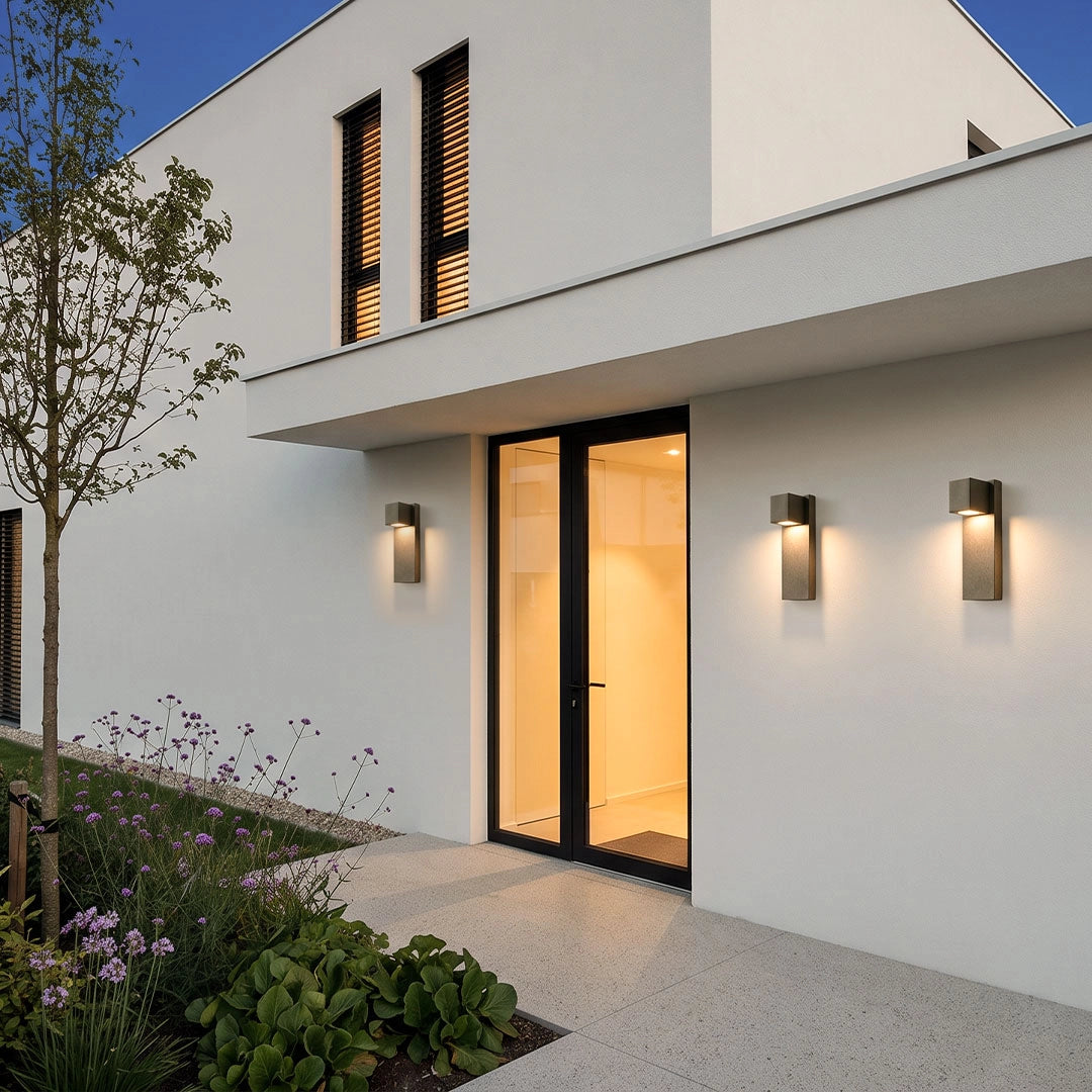 Outdoor stone wall lighting arranged in a row on a white exterior wall outside a modern home.