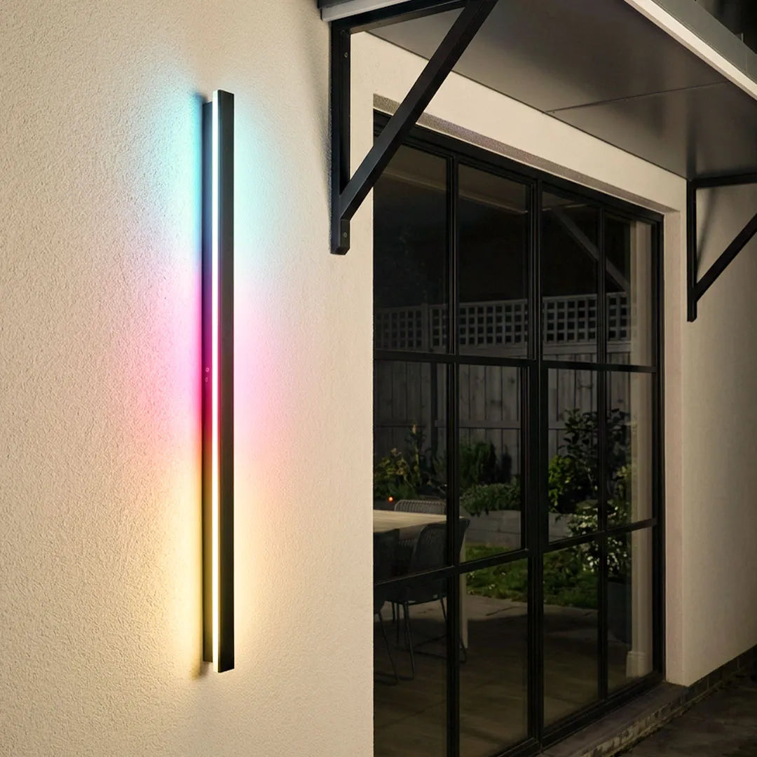 Outdoor strip wall light mounted beside a glass door, creating a vertical multicolor glow on a modern exterior wall.