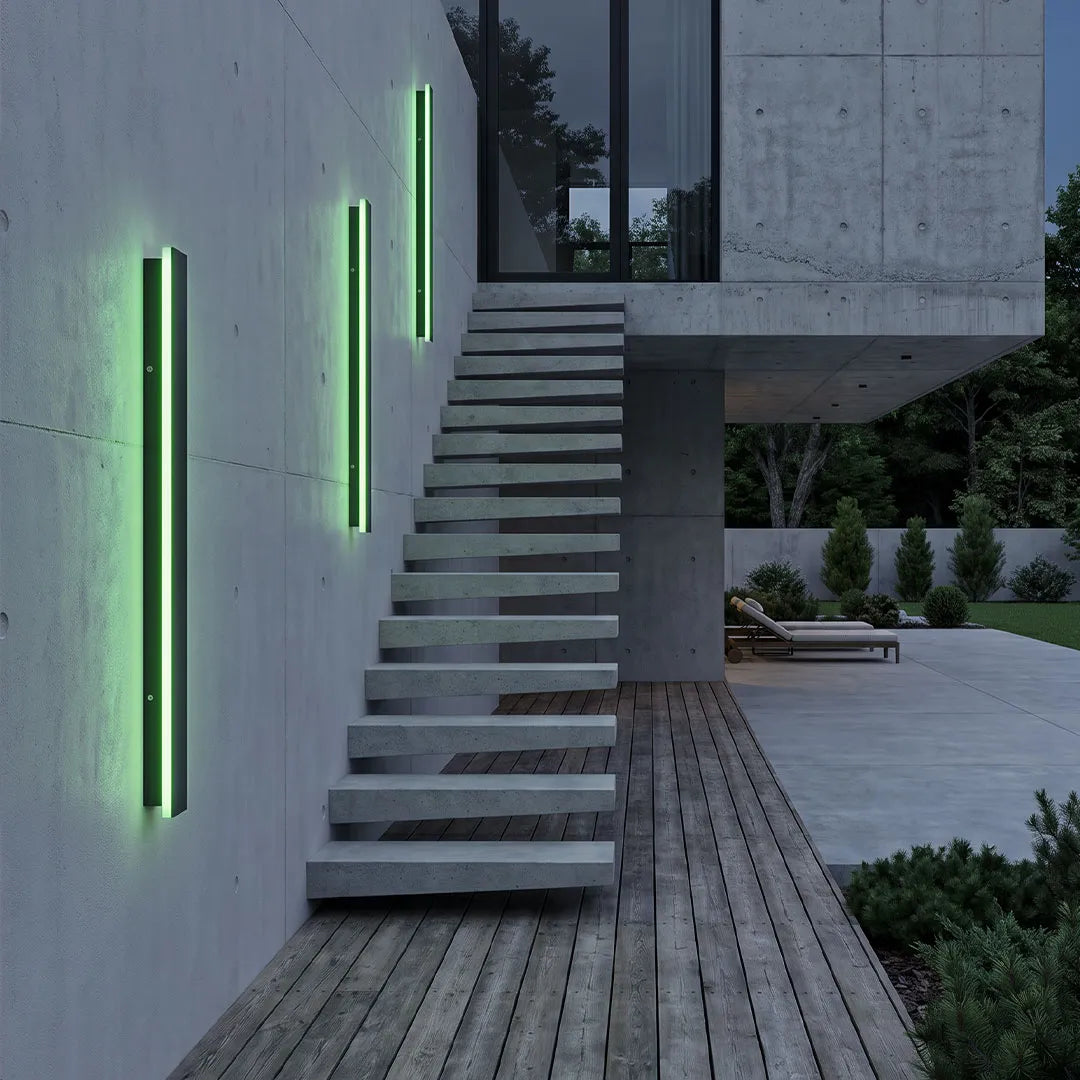 Outdoor strip wall lights installed along a concrete staircase wall, casting green vertical illumination in a modern outdoor space.