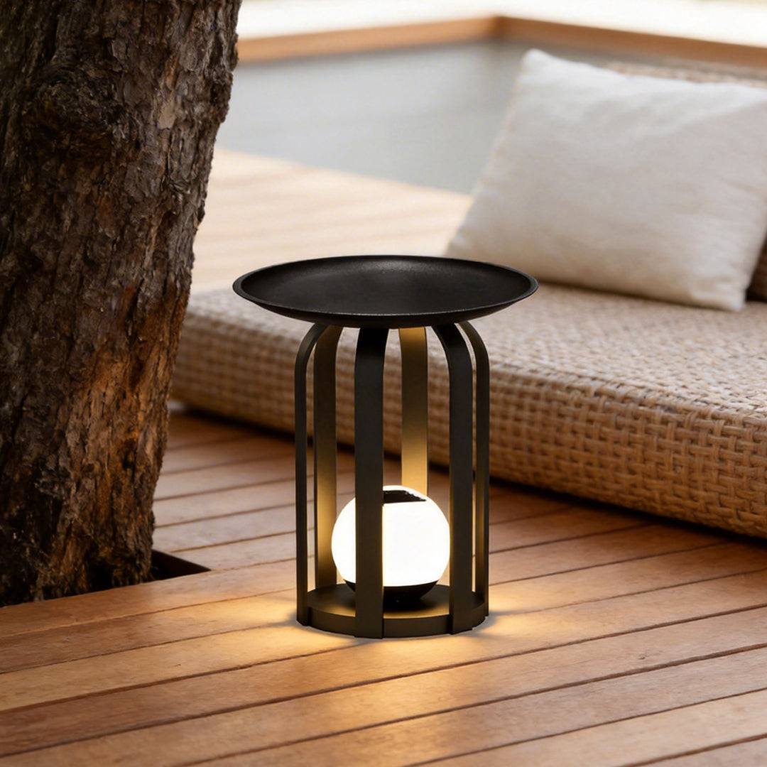 Outdoor tray floor lamp with a black metal frame, providing warm illumination on a wooden deck.