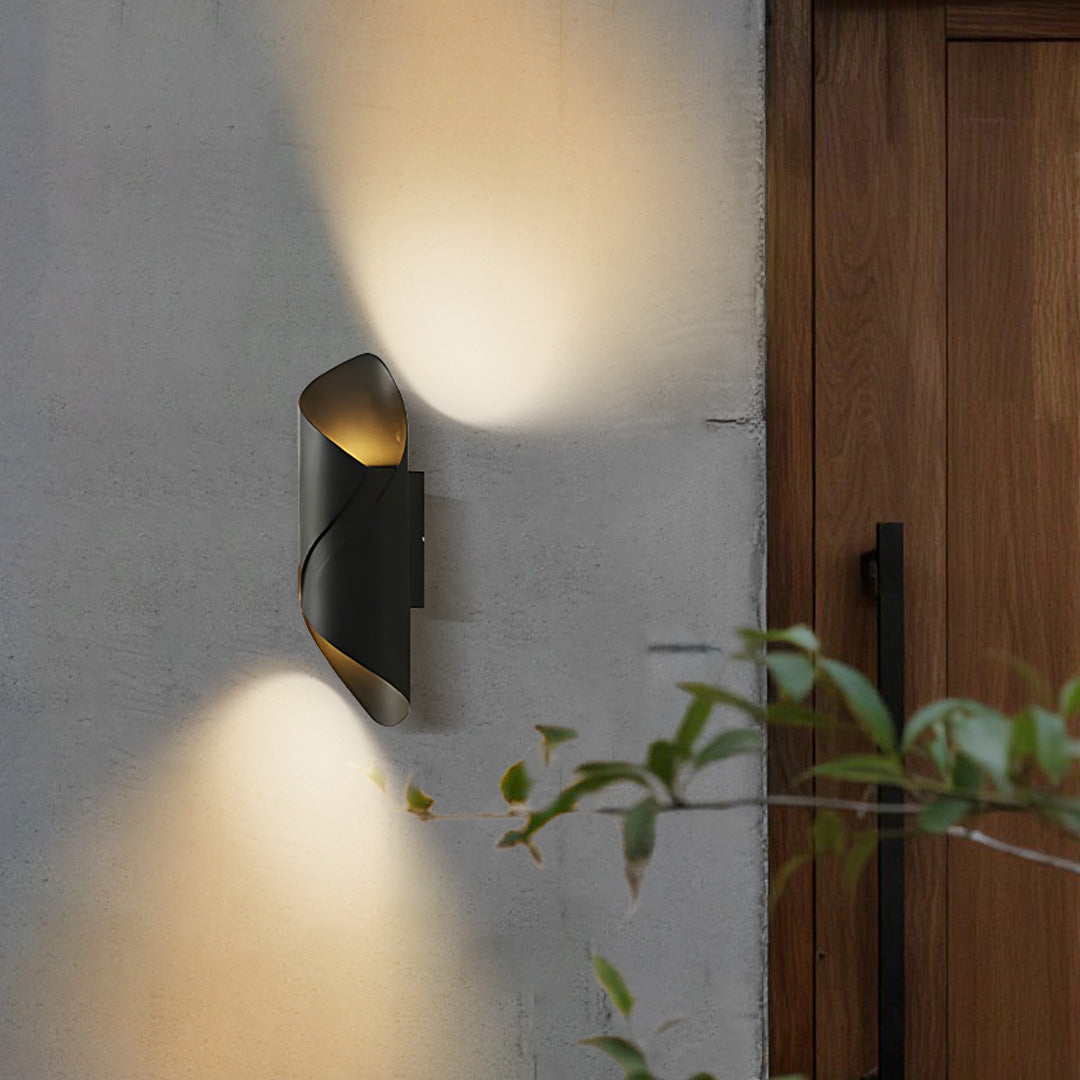 Outdoor up down wall light with modern black and gold design, mounted beside wooden door.