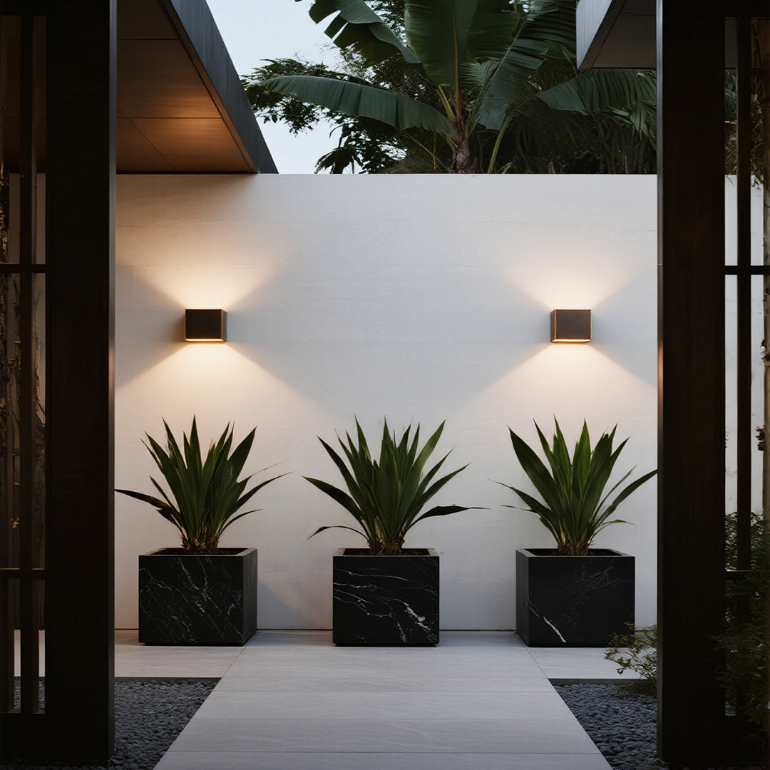 Outdoor up down wall light illuminating a modern building entrance with potted plants.