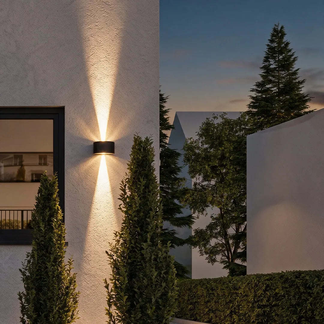 Outdoor up down wall light on a white exterior wall, creating dramatic warm light beams at dusk.