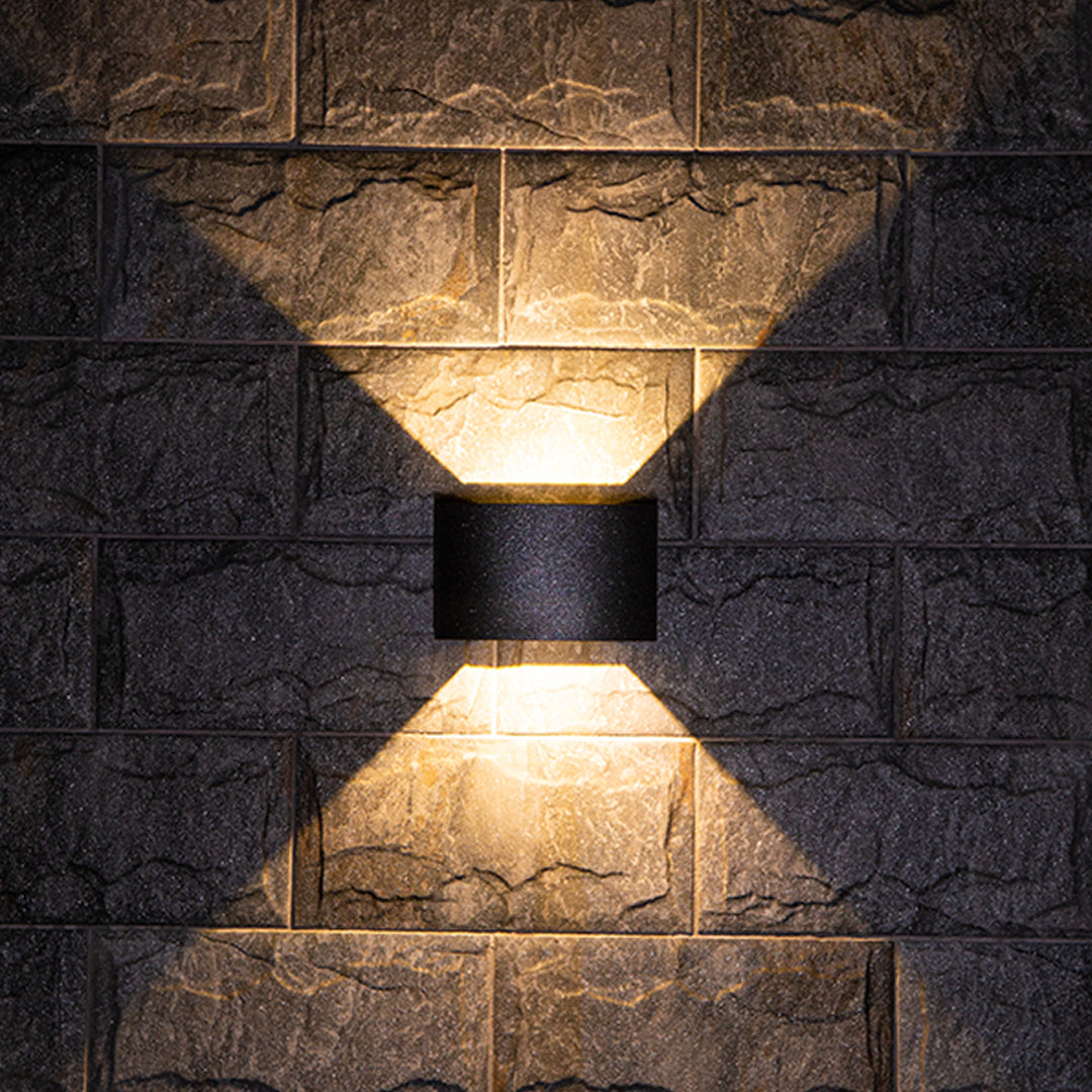 Outdoor up down wall light casting warm golden glow on textured stone surface