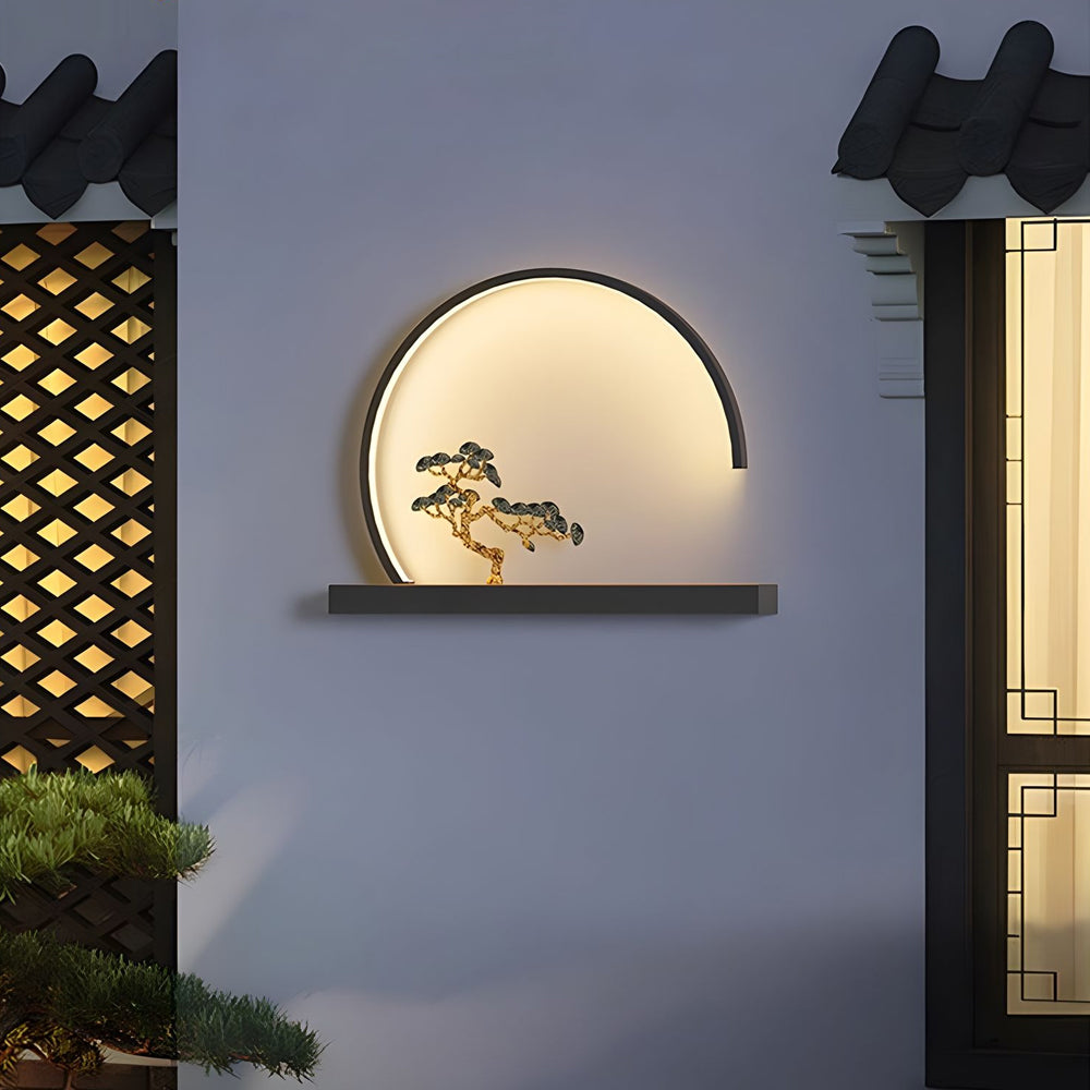 Contemporary outdoor wall fixture with illuminated circular frame and bonsai tree accent mounted on modern building exterior