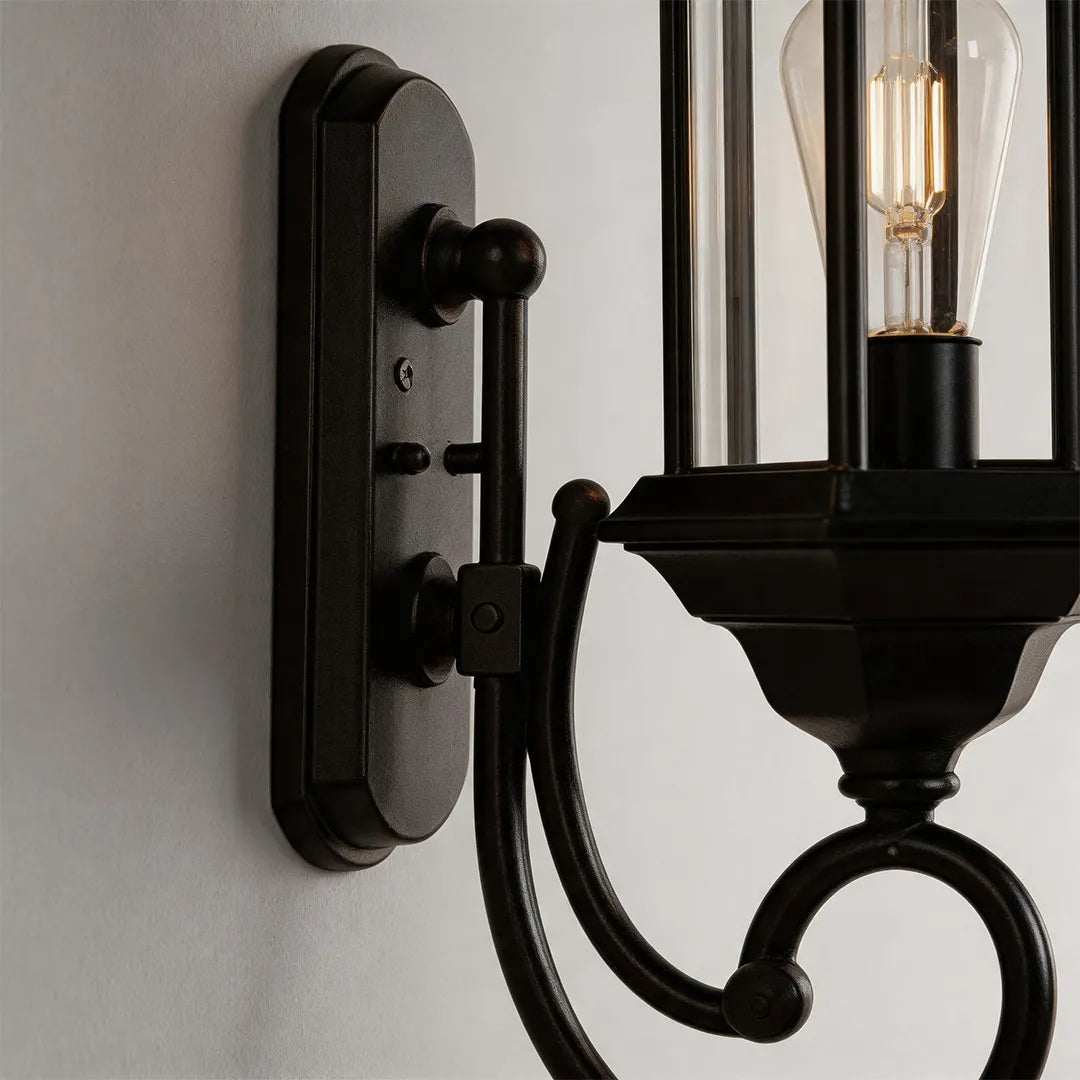 Outdoor wall lantern light hardware detail showing the black wall plate, curved arm, and metal frame.