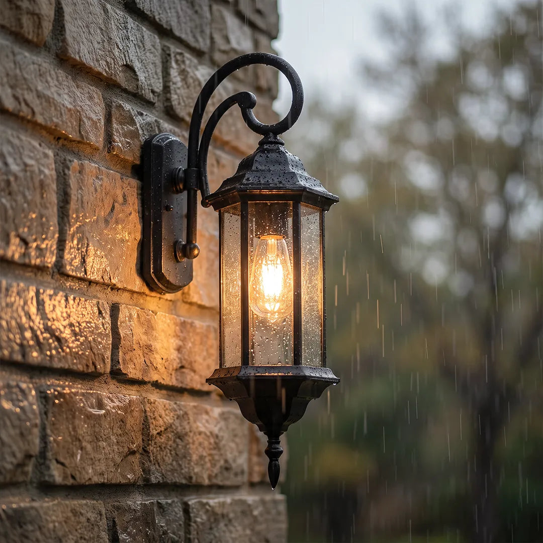 Outdoor wall lantern light close-up glowing in the rain on a brick wall with clear glass panels.