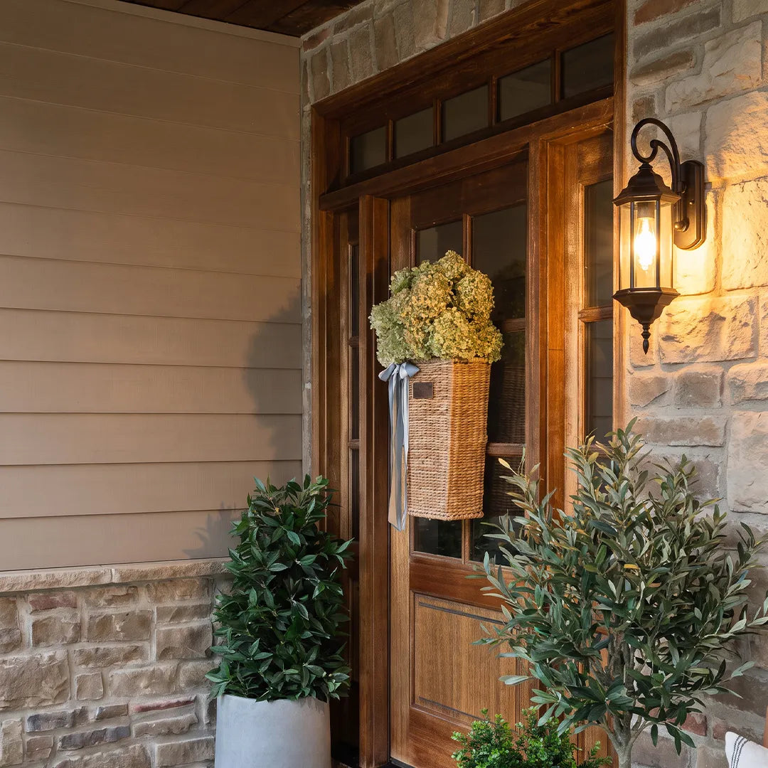 Outdoor wall lantern light flanking a stone entryway with a wooden front door and tall planter basket.