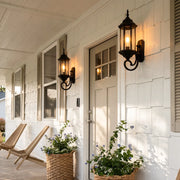 Outdoor wall lantern light mounted beside a white entry door on a covered porch with black metal finish.
