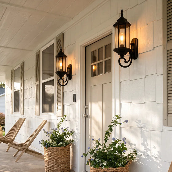 Outdoor wall lantern light mounted beside a white entry door on a covered porch with black metal finish.