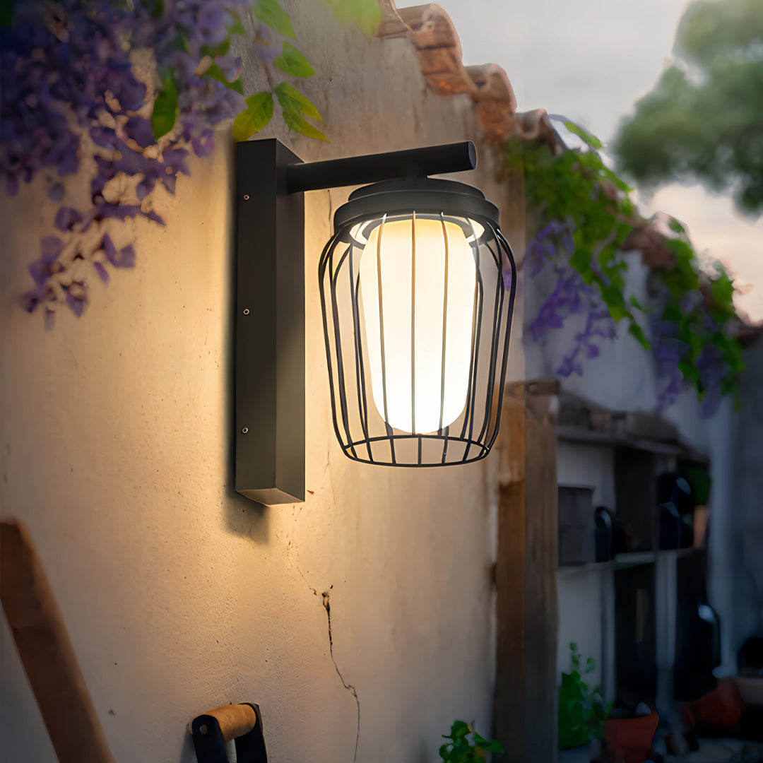 Outdoor wall lantern sconce mounted near garden foliage, featuring ribbed glass and warm architectural lighting.