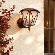 Outdoor wall light for house casting warm glow on textured beige stucco beside autumn foliage