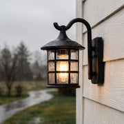 Outdoor wall light lantern mounted on exterior siding with a curved arm and seeded glass shade.