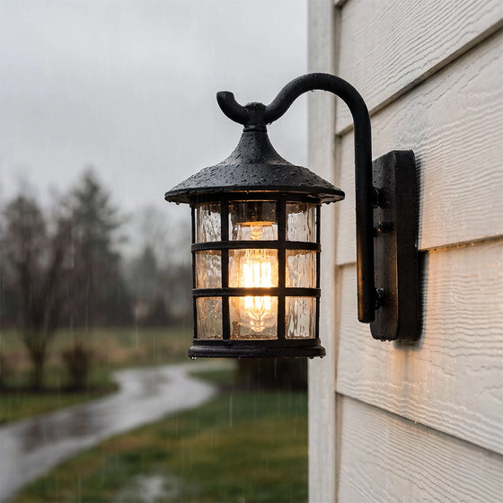 Outdoor wall light lantern mounted on exterior siding with a curved arm and seeded glass shade.