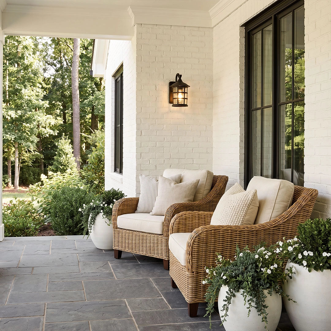 Outdoor wall light lantern mounted on a white brick porch wall beside woven outdoor seating.