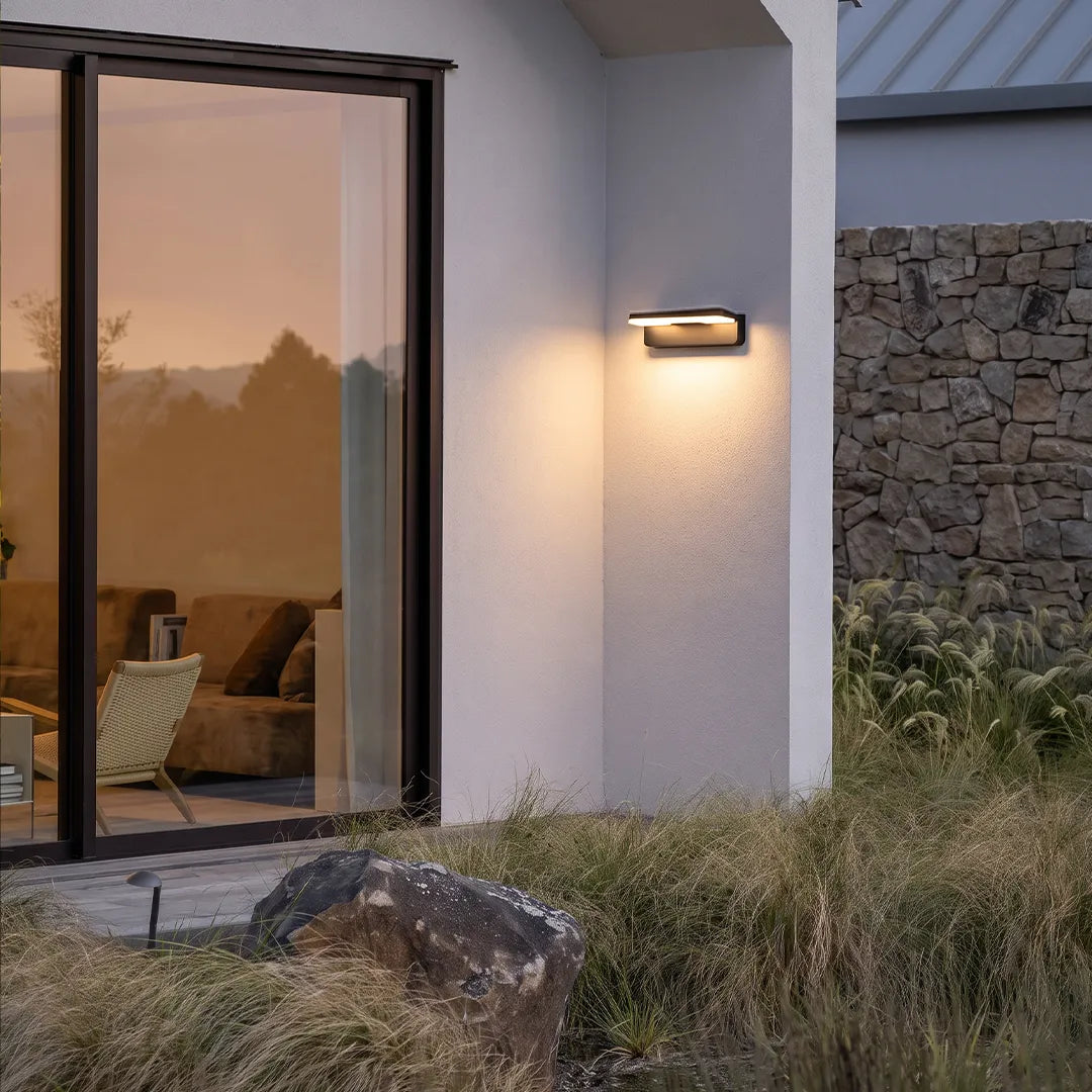 Outdoor wall light with warm glow beside patio glass door and landscaping