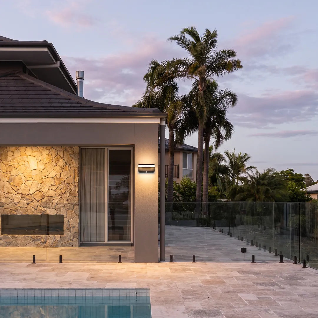 Outdoor wall light illuminating modern poolside patio and stone house exterior